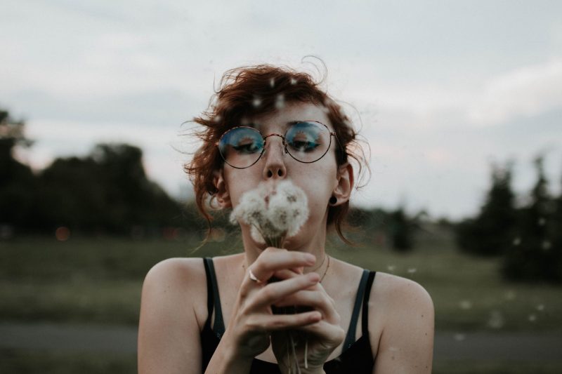 selective focus photography of woman blowing dandelion flower