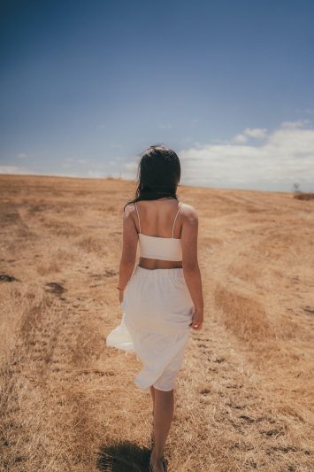 back view of a woman wearing white skirt walking in a summer field