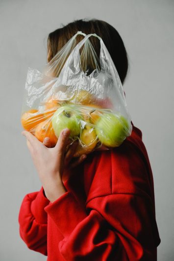 person carrying a plastic bag full of fruits