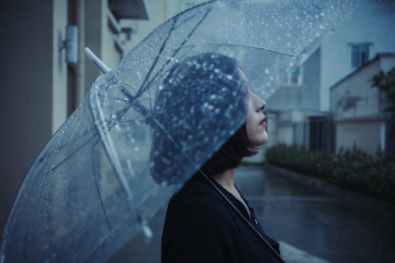 brunette woman with transparent umbrella on rainy day