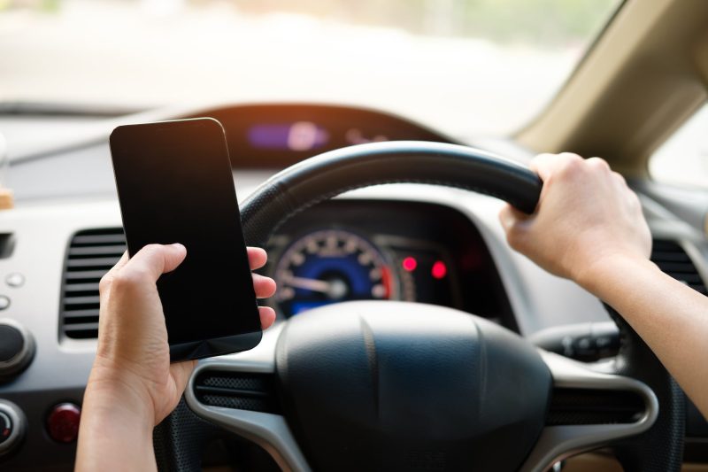 person holding black smartphone and vehicle steering wheel