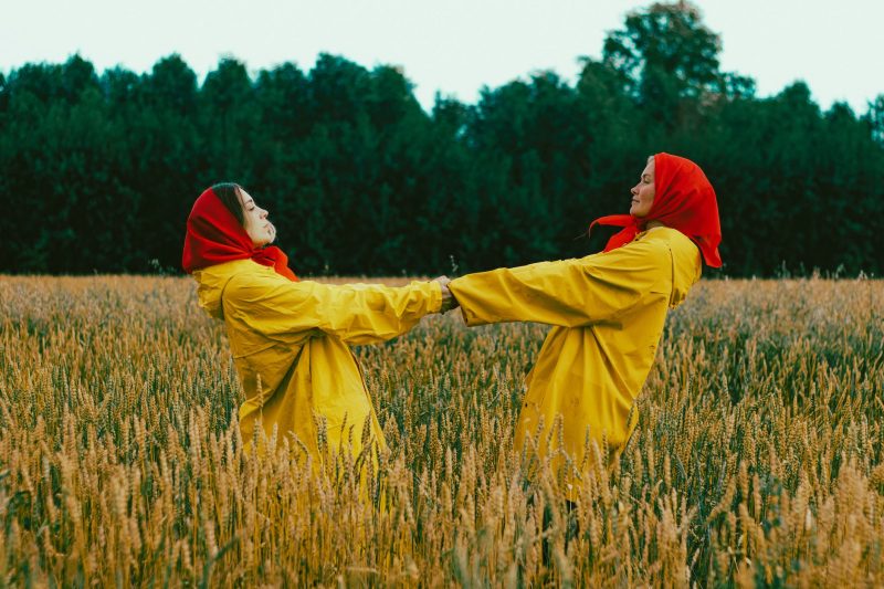 women in yellow coats and red handkerchiefs dancing in field