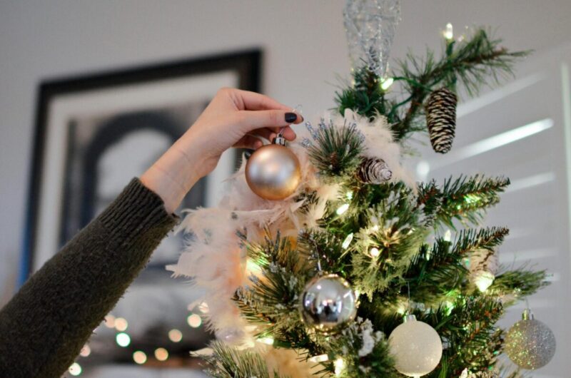person holding beige bauble near christmas tree