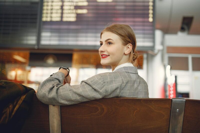 side view of positive female manager waiting for flight on wooden seat in airport