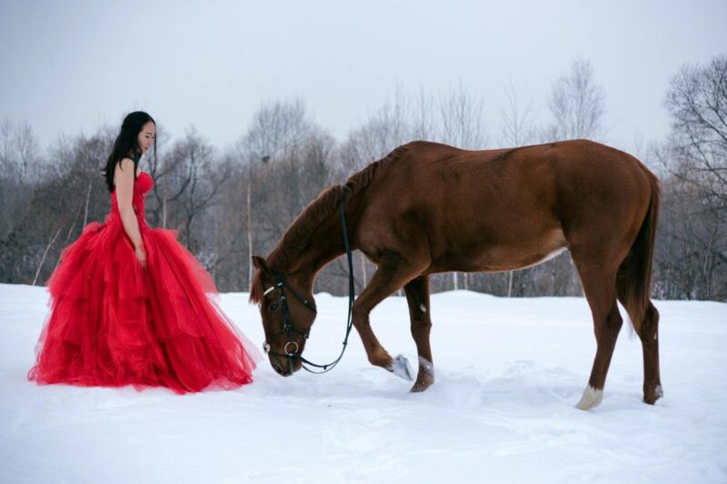young woman in long red dress watching horse
