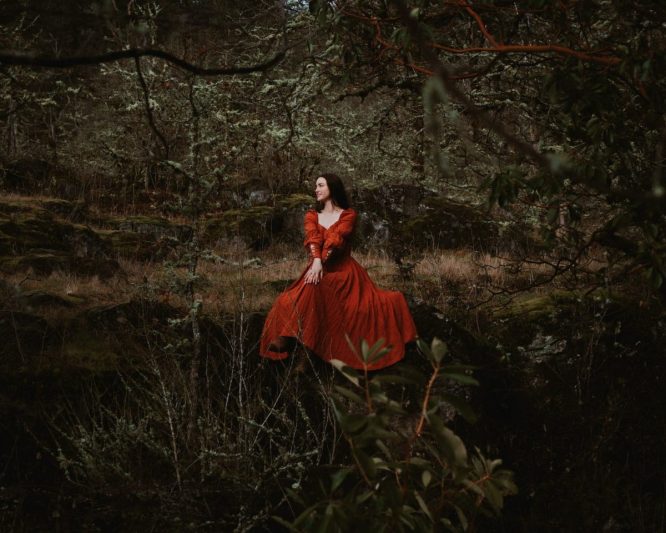 woman in a red medieval dress sitting on a rock in the forest
