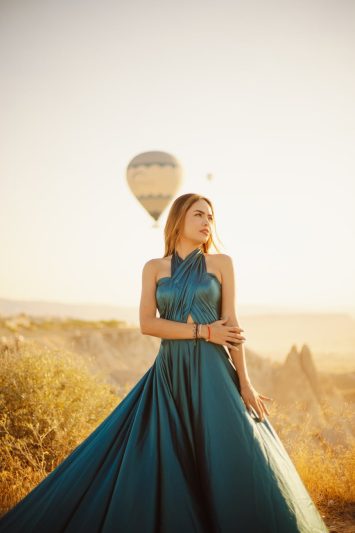elegant woman in a blue maxi dress posing on the background of hot air balloons flying in cappadocia
