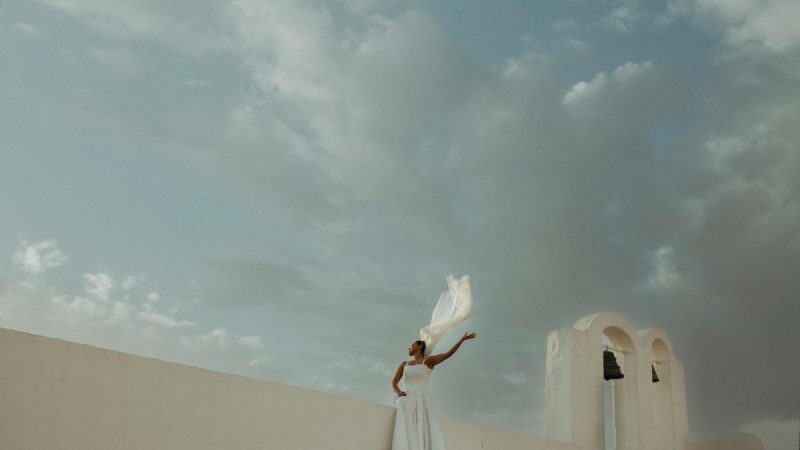 bride standing on a rooftop of a church next to bells