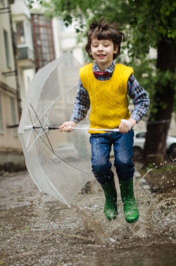 boy holding umbrella while smiling and running