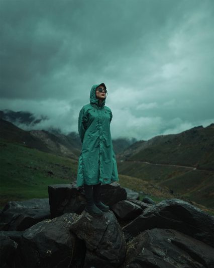 woman in raincoat in valley in mountains