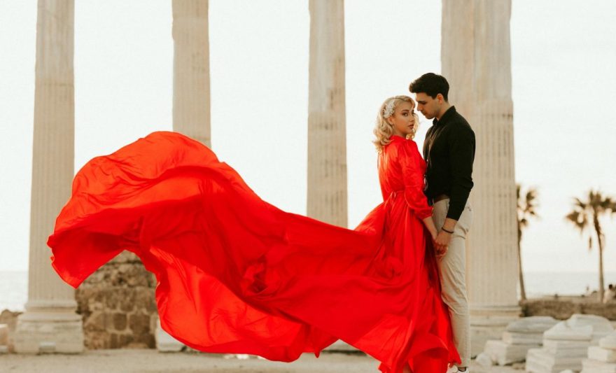 a man holding hands with a woman in a red gown