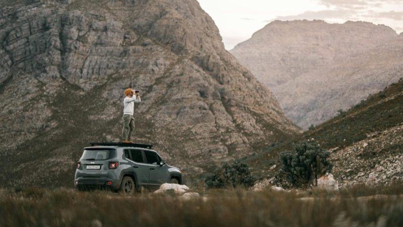 a man using binoculars while standing on an suv in the outdoors