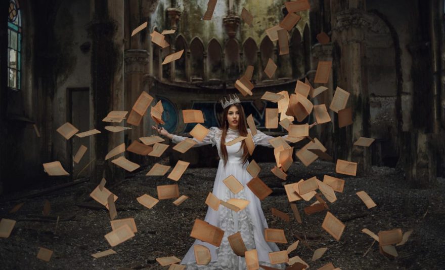 woman in a costume and a crown with old yellow book pages flying around her