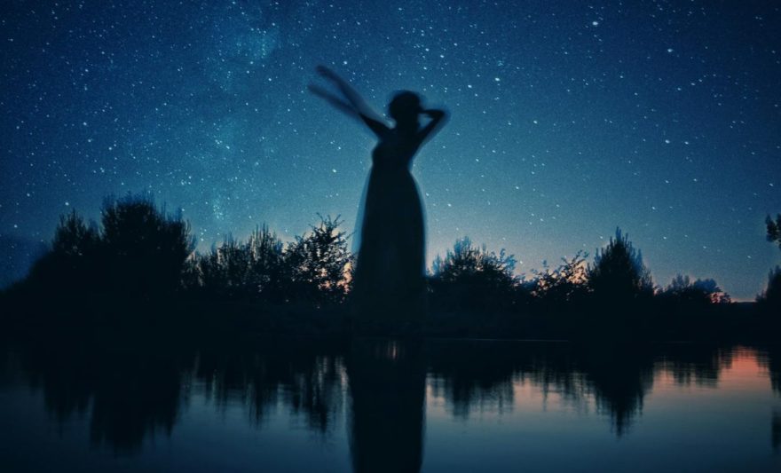 silhouette of woman standing on rock near body of water during night time