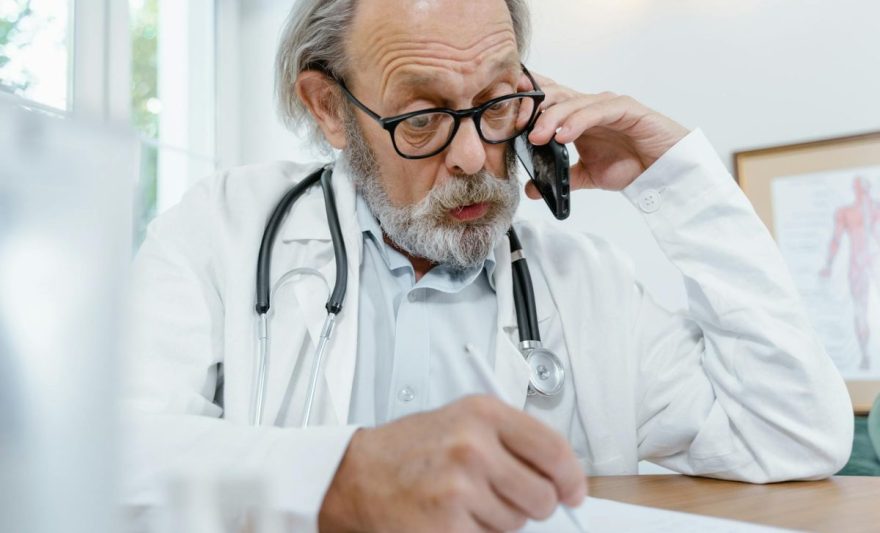 man in white scrub suit holding black and silver stethoscope