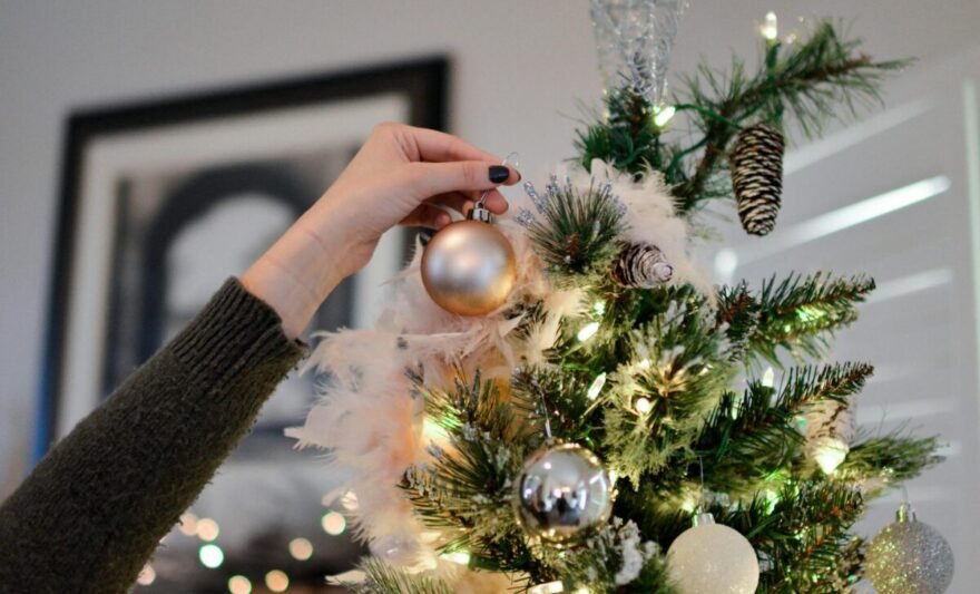 person holding beige bauble near christmas tree