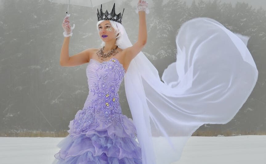 female with umbrella in crown and dress on snowy field