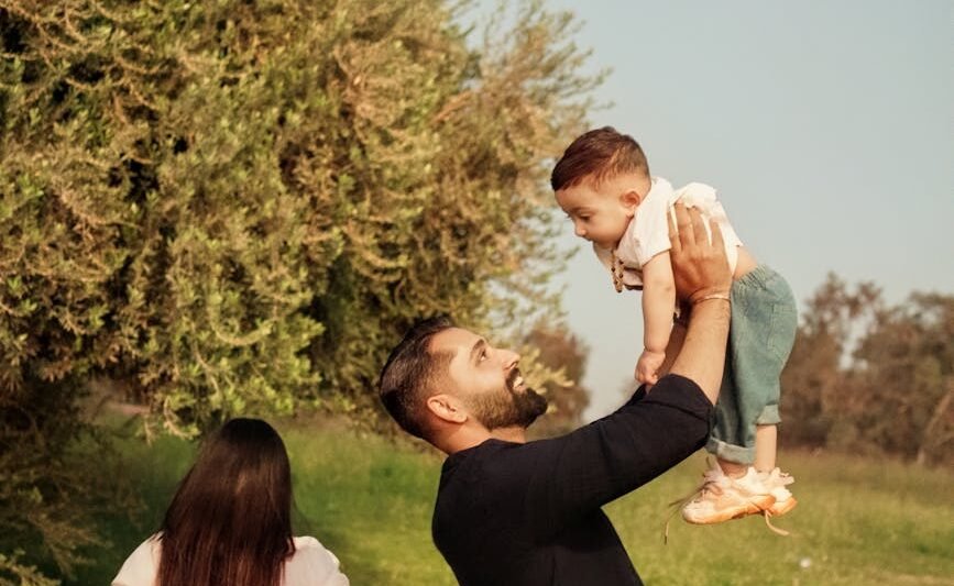 father lifting child in sunny park