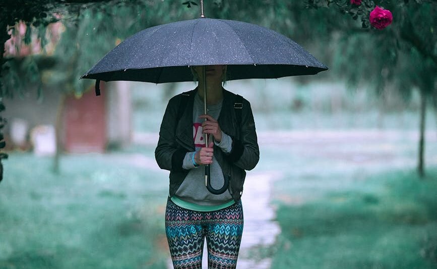 crop woman in activewear standing under umbrella on rainy day