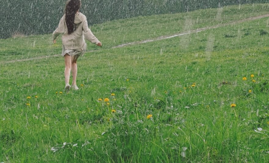 woman enjoying the rain outside a grass field