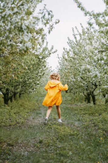 rear view of woman in yellow coat walking in orchard