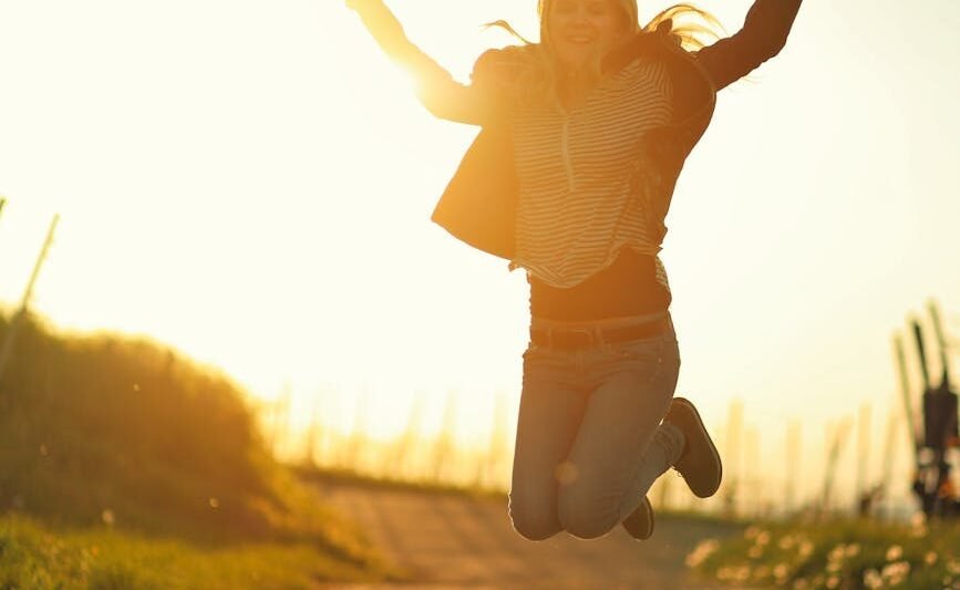 woman in jump over rural road at sunrise