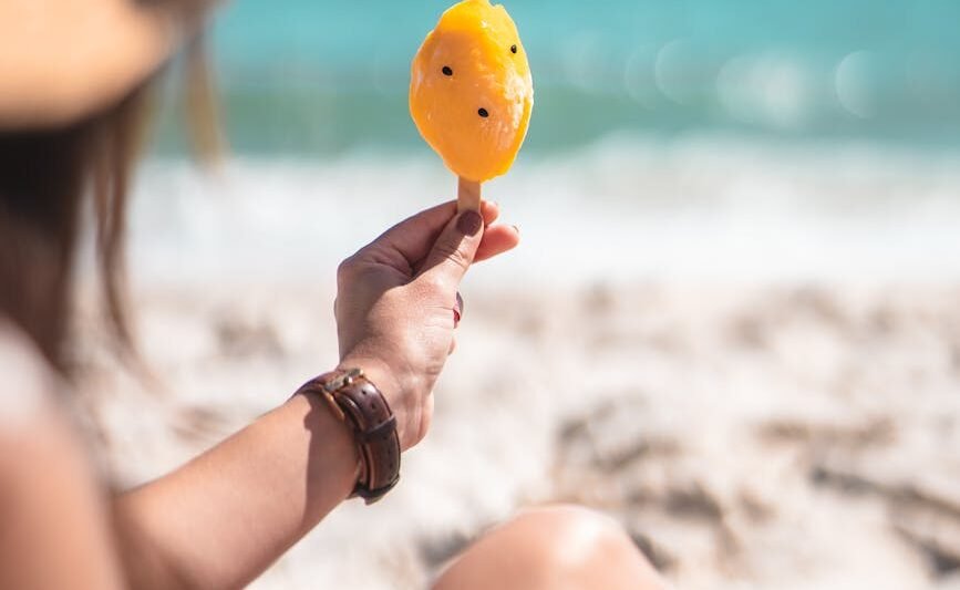 shallow focus photo of person holding a yellow popsicle