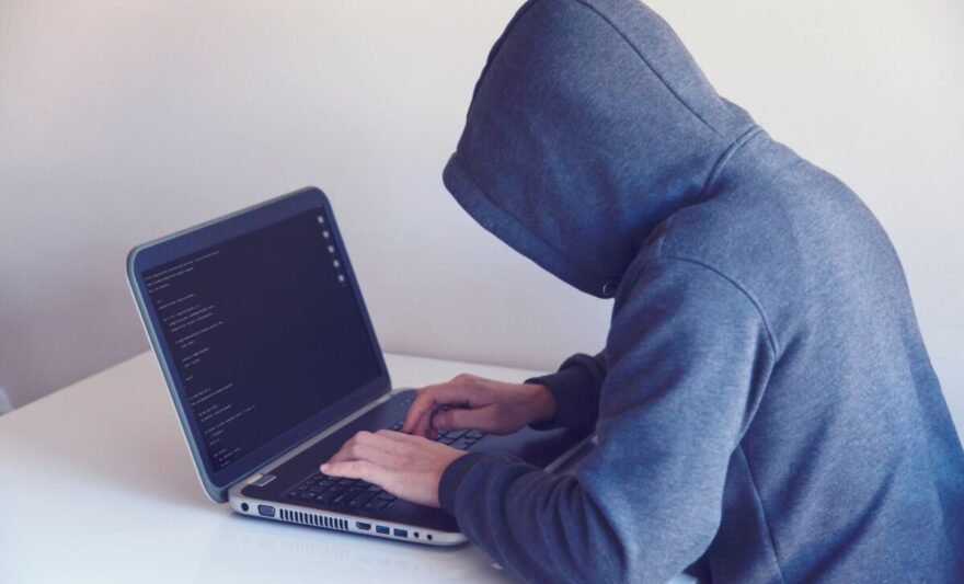 anonymous hacker with on laptop in white room