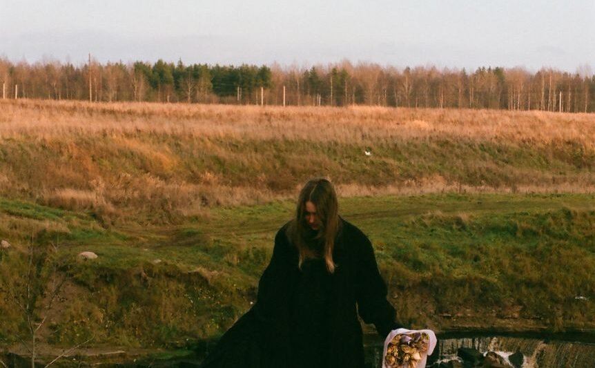woman in black dress standing near a river with a bouquet of flowers
